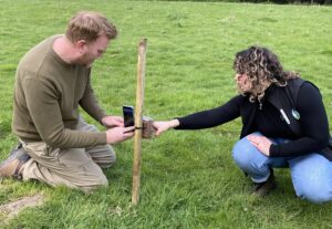 An Operation Turtle Dove adviser and a volunteer crouch on the ground setting up a trail camera